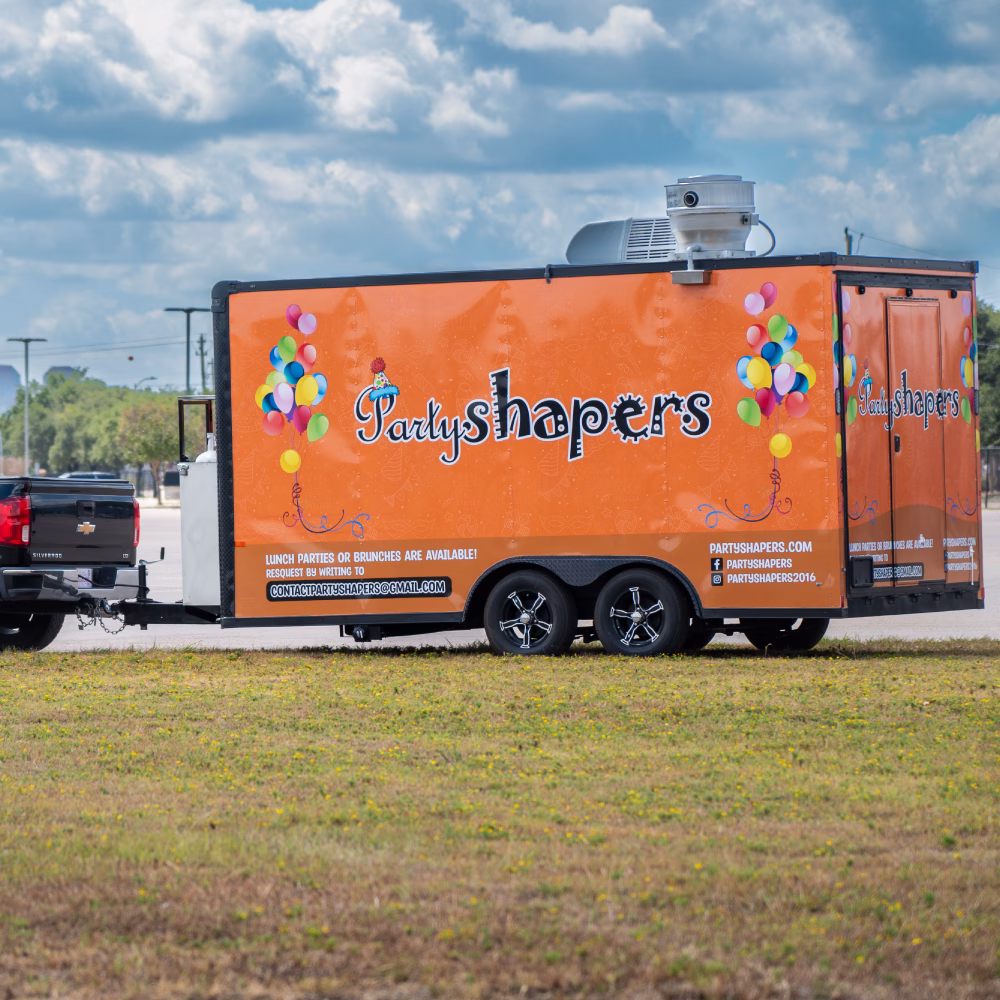 Custom-built concession trailer with an orange vinyl wrap sitting in a field.