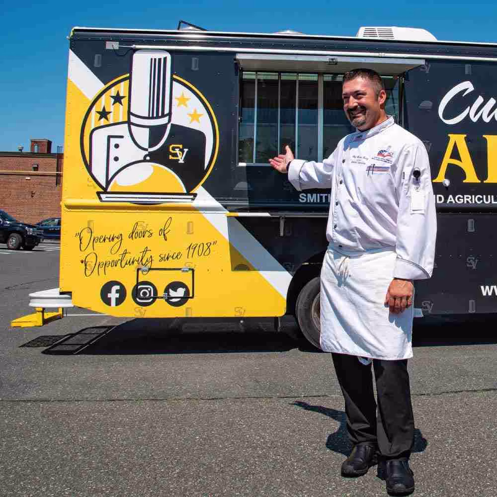 Smith Tech chef in front of their custom-built food truck with a black and yellow culinary-themed vinyl wrap.
